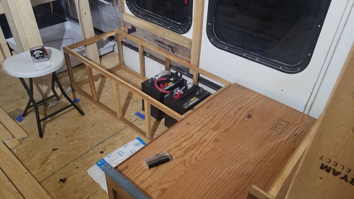 Two 12V batteries wired together inside a plywood-framed battery bay, early in construction.