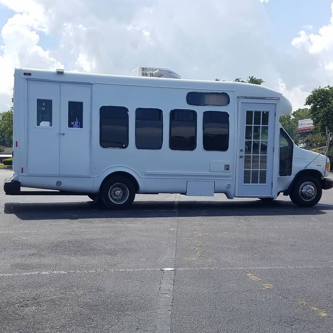 Driver's side profile of the finished white E-450 box-conversion camper parked in a lot, doors and windows visible.