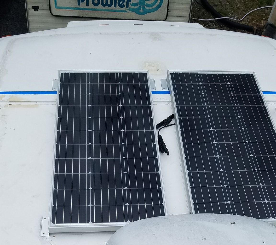 Two solar panels mounted side by side on a white camper roof, leads joined between them.
