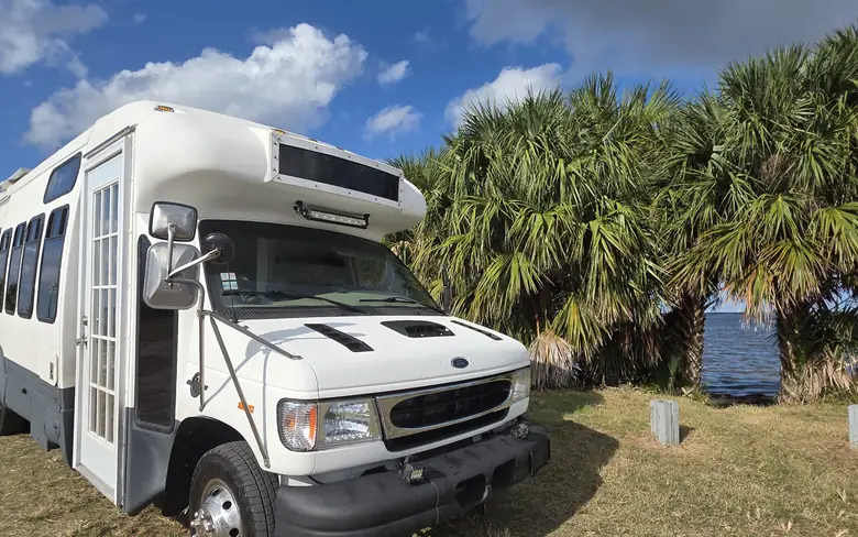 Our finished Ford E-450 bus conversion, white with a grey lower third, parked under palms by the water in Florida