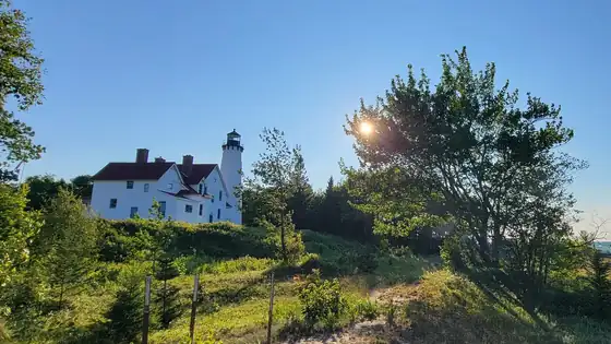 The white brick Point Iroquois lighthouse and keeper's house seen across the dunes at sunset