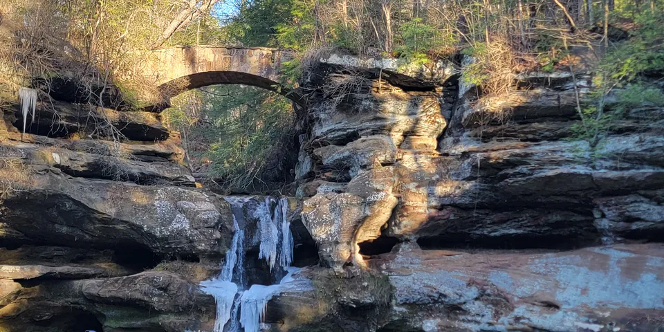 A partly frozen waterfall below a stone arch bridge in a sandstone gorge