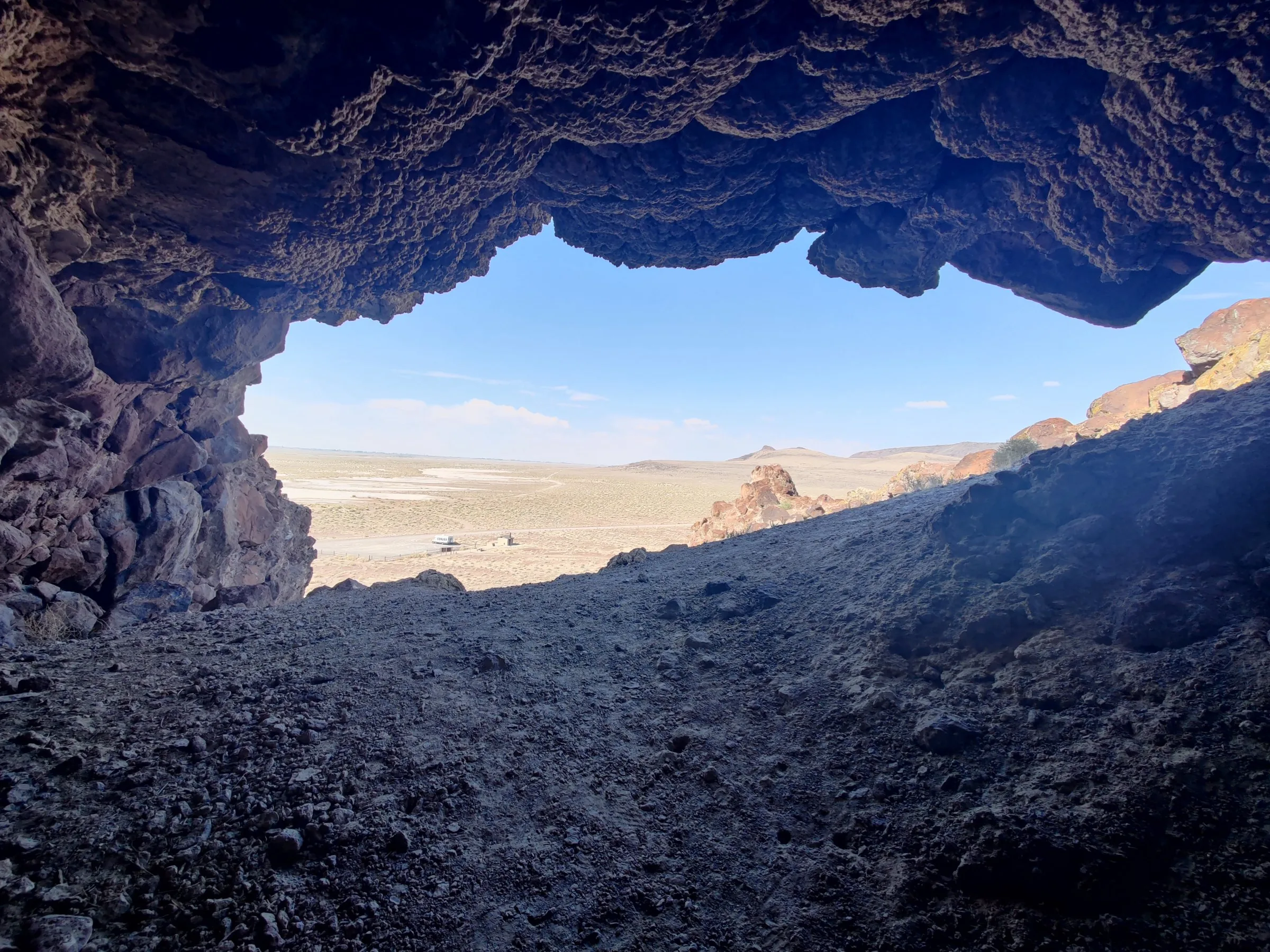 Looking out from inside Hidden Cave near Fallon, Nevada — the rock mouth framing open high desert and the valley floor beyond
