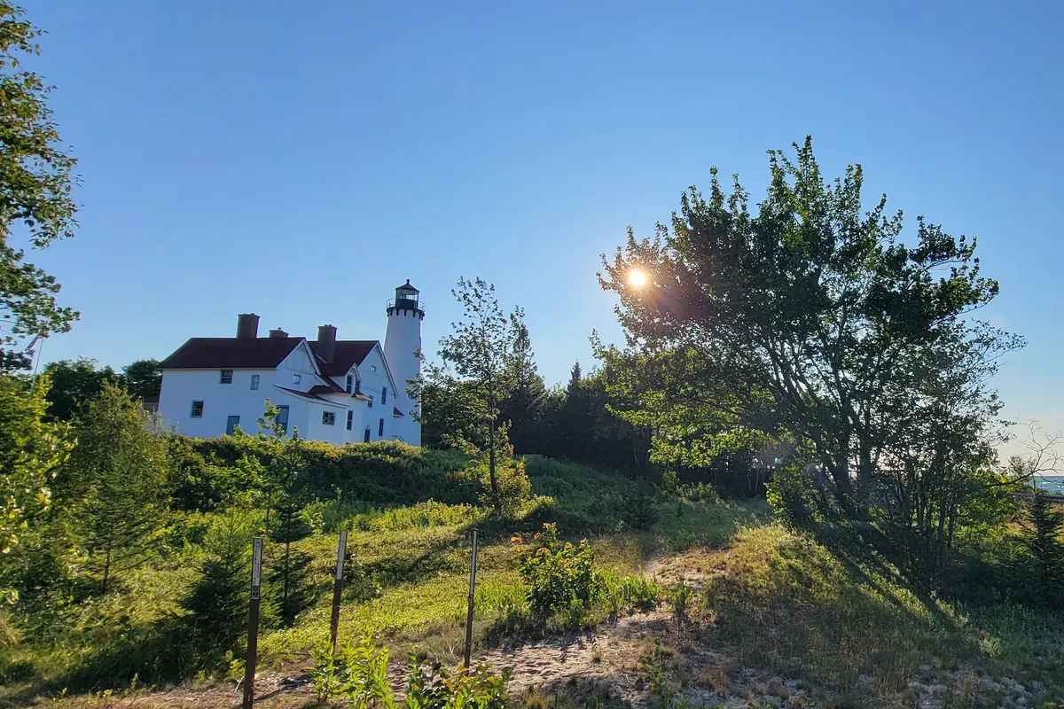 The white brick Point Iroquois lighthouse and keeper's house seen across the dunes at sunset